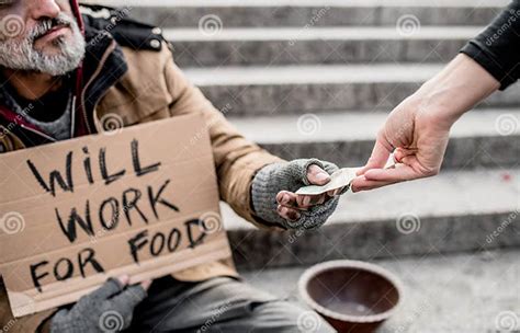 A Midsection Of Woman Giving Money To Homeless Beggar Man Sitting In