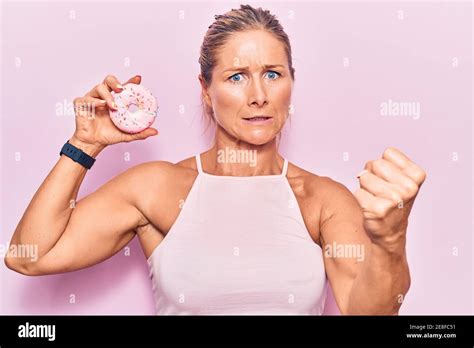 Femme blonde caucasienne d âge moyen portant des vêtements sportifs et tenant le beignet de