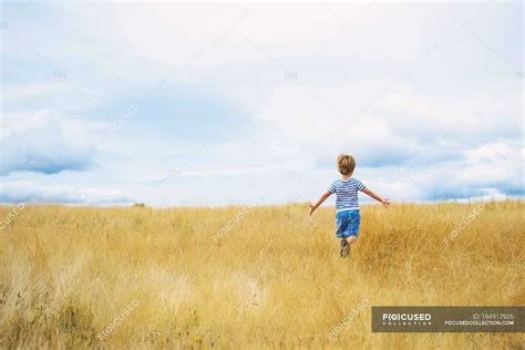 Little boy running through field under cloudy sky — innocence, kid ...