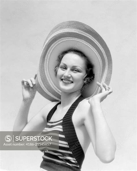 1930s Portrait Smiling Woman In Straw Hat And Striped Halter Top Holding The Hat On With Her