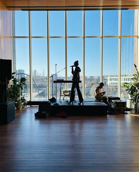 Two People Standing On Stage In Front Of Large Windows With Cityscape