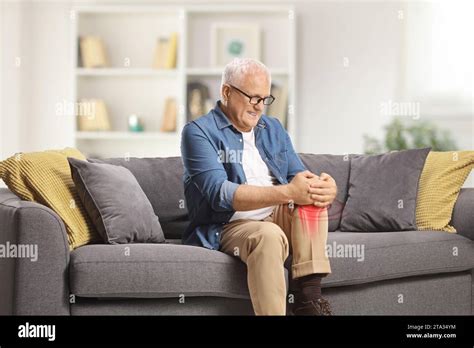 Mature Man In Pain Sitting On A Sofa At Home And Holding His Red