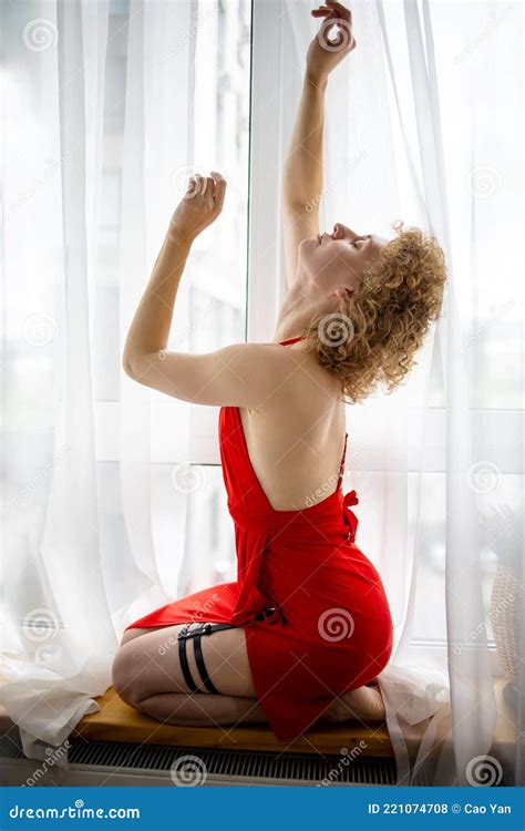 Beautiful Blonde Woman In Red Dress Relaxing Near Window Stock Photo