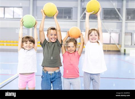 Cheerful Students With Arms Raised Holding Ball Standing Together At