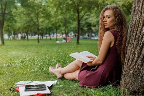 Premium Photo Portrait Of Young Woman Reading Book While Sitting On Field