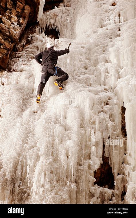 Man Climbing Frozen Waterfall Against Rock Formation Stock Photo Alamy