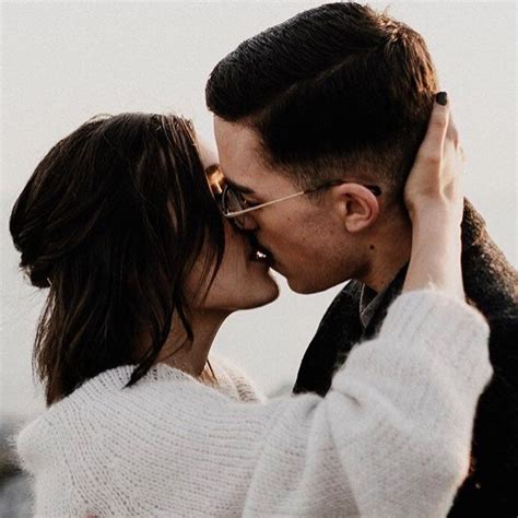 A Man And Woman Kissing In Front Of The Ocean