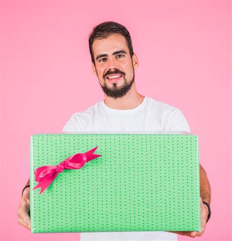 Free Photo Man Holding Large Gift Box With Bow Against Pink Background