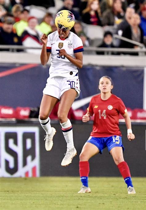 Two Women Are Playing Soccer In Front Of An Audience And One Is Jumping