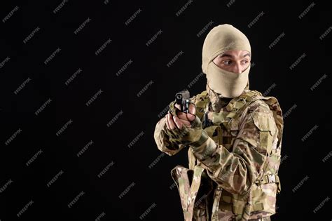 Вид спереди молодого солдата в форме, прицеливающегося из пистолета на ...