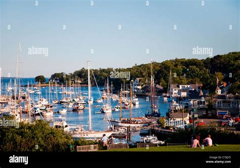 A Couple Sits On A Grassy Hilltop Overlooking The Harbor Below Stock