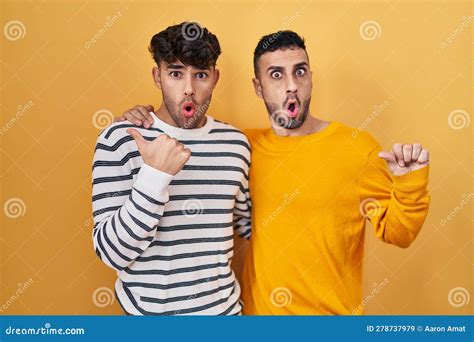 Jeune Couple Gay Hispanique Debout Sur Fond Jaune Surpris Pointant Main Sur Le Côté Ouvert