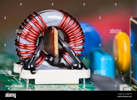 Ferrite Core Inductor On White Holder And Colored Capacitors On Green Circuit Board Close Up Of