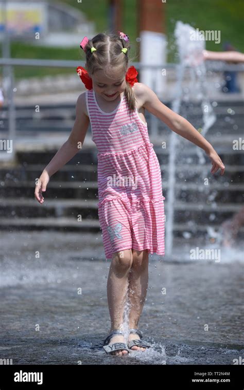 Strong heat in the city: little girl playing with fountain water jets ...