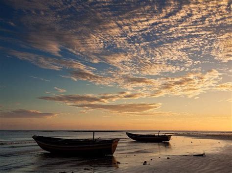 Two Boats Sitting On Top Of A Sandy Beach Under A Cloudy Blue And