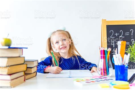 Happy Cute Industrious Child Is Sitting At A Desk Indoors Stock Photo