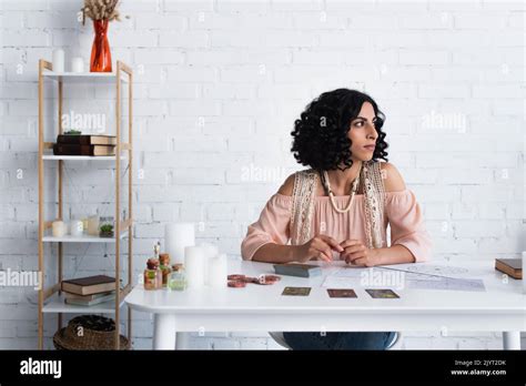 Brunette Fortune Teller Looking Away While Sitting Near Tarot Cards And