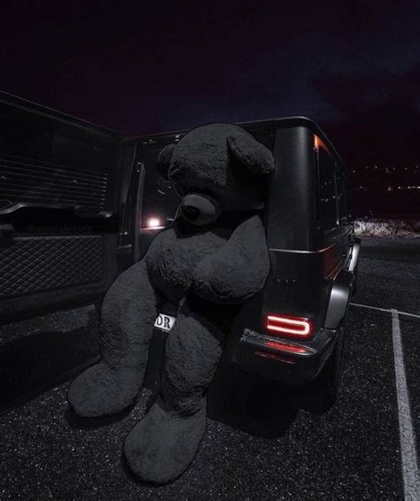 A Large Black Teddy Bear Sitting On The Back Of A Truck In Parking Lot