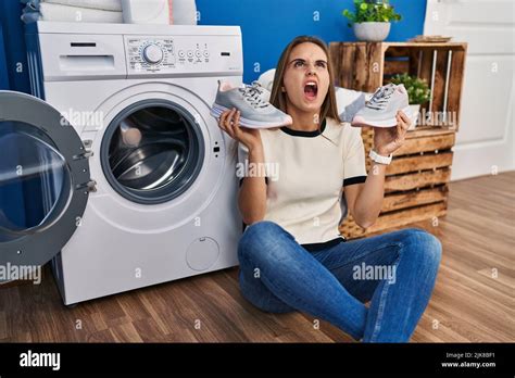 Young Woman Putting Sneakers In Washing Machine Angry And Mad Screaming