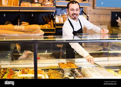 Male Shop Assistant Demonstrating Fresh Delicious Pastry In Bakery