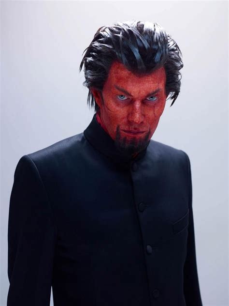 A Man With Red Paint On His Face Wearing A Black Suit And Tie Standing