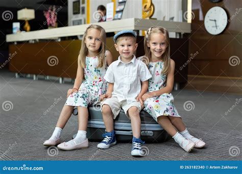 Twin Sisters And Brother Sitting On A Suitcase In A Hotel Stock Photo