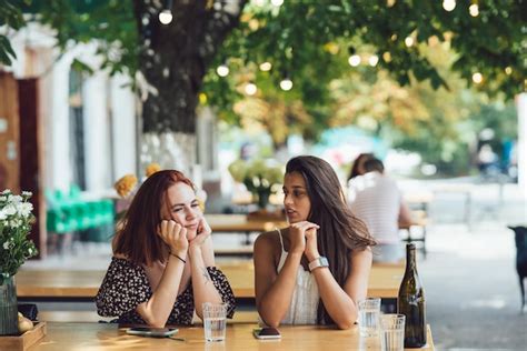 Premium Photo Two Young Beautiful Women Girlfriends Talking In An Outdoor Cafe