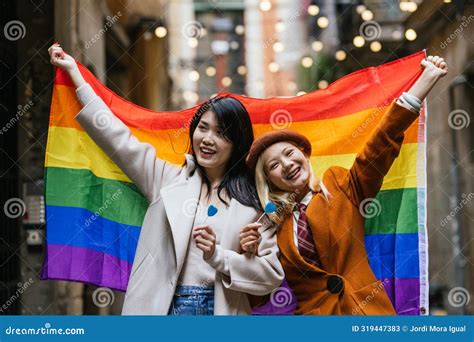 Happy Asian Lesbian Couple Smiling While Holding A Lgbt Rainbow Flag