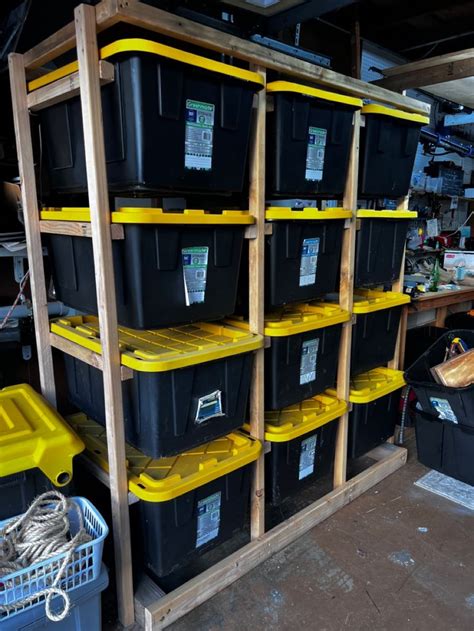 Several Black And Yellow Bins Are Stacked On Wooden Shelves In A Garage