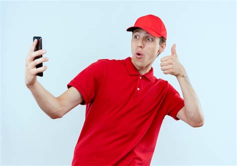 Jovem entregador de uniforme vermelho e boné segurando smartphone