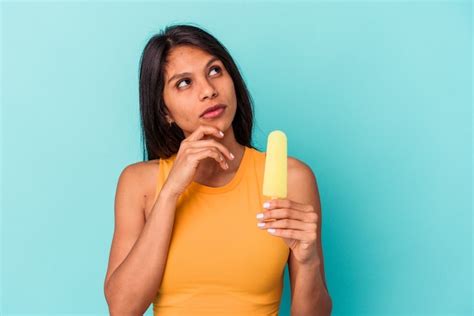 Mujer latina joven con helado aislado sobre fondo azul mirando hacia los lados con expresión