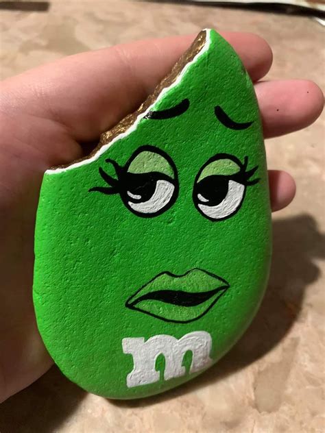 A Hand Holding A Green Rock With An Angry Face Painted On It