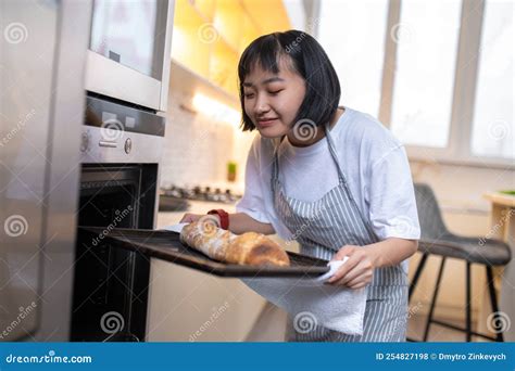 Young Housewife Baking Something In The Oven And Looking Busy Stock