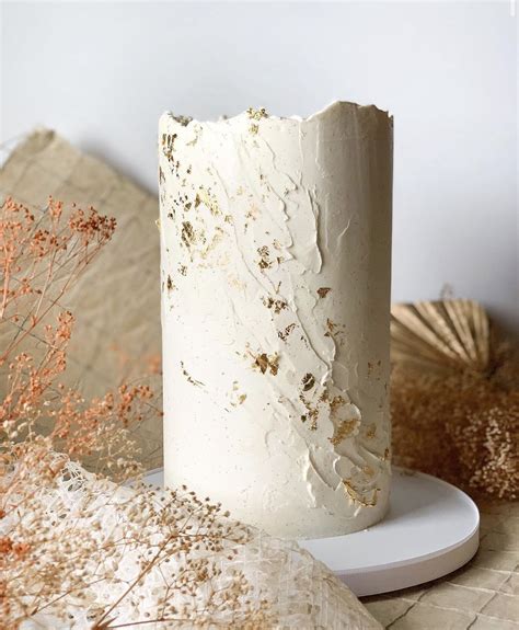 A White Frosted Cake Sitting On Top Of A Plate Next To Dried Flowers