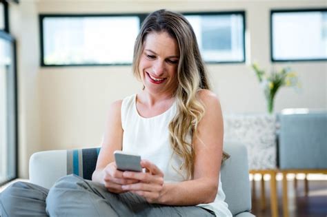 Premium Photo Smiling Woman Sitting On The Couch Looking At Her Mobile Phone