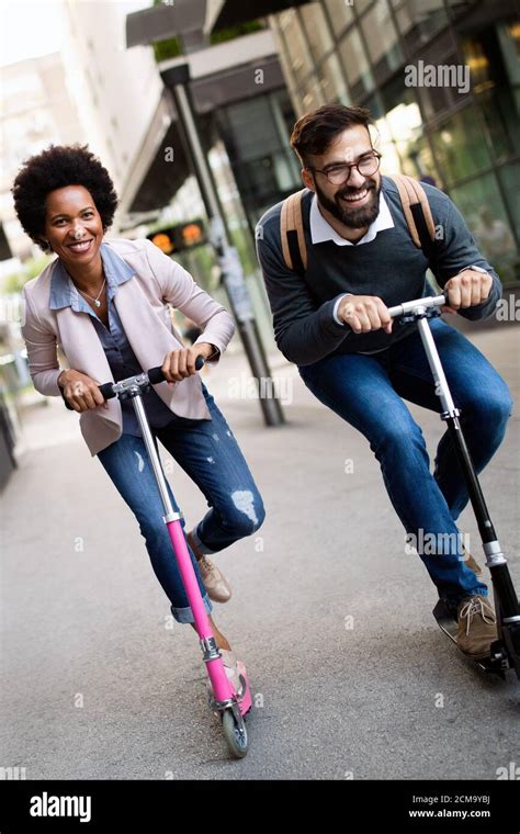 Two smiling business people driving electric scooter going to work ...