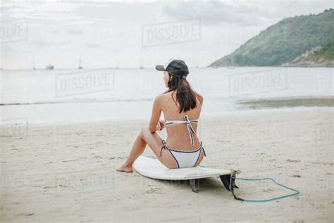 Back View Of Surfer In Bikini Sitting On Surfboard On Beach At Ocean Stock Photo Dissolve