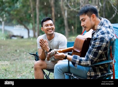 LGBTQIA Gay Couple Camping Together In Woods For Holidays And Relax On Guitar Together Stock