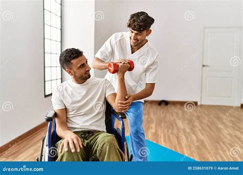 Two Hispanic Men Physiotherapist And Patient Sitting On Wheelchair Having Rehab Session Using