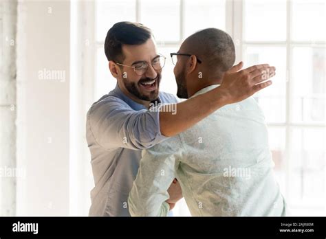 Smiling Male Friends Embrace Tap Shoulder Meeting Indoors Stock Photo
