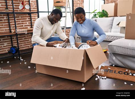 Man And Woman Couple Unboxing Cardboard Box Sitting On Floor At New