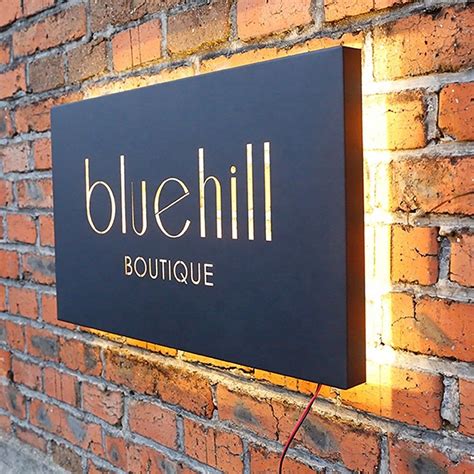 The Blue Hill Boutique Sign Is Lit Up Against A Brick Wall With An