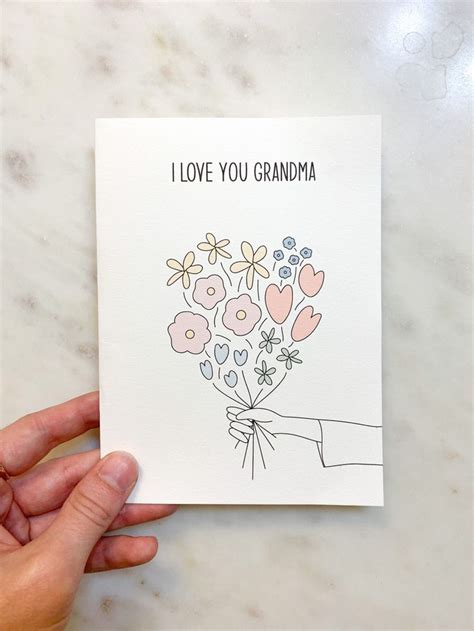 A Hand Holding A Card With Flowers On It That Says I Love You Grandma