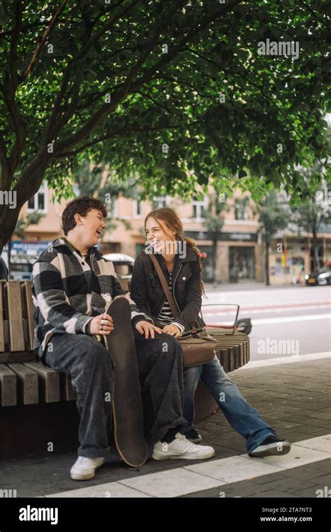 Happy Male And Female Teenage Friends Laughing While Sitting On Bench