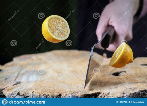 Hand With Knife Slicing A Lemon In Half On The Wooden Board Stock Image