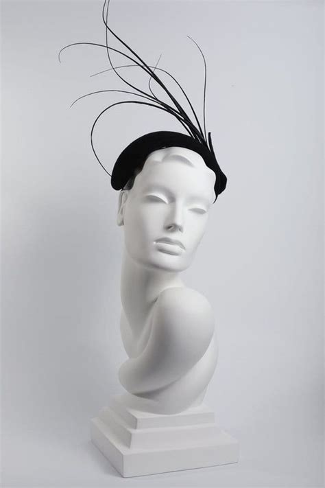 A White Mannequin Head Wearing A Black Hat With Feathers On It S Head