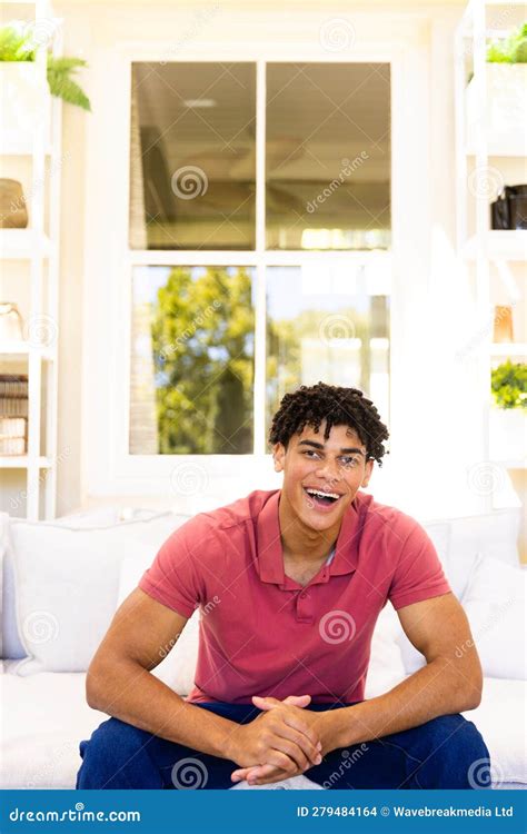 Portrait Of Happy Biracial Man Sitting On Sofa In Living Room Smiling