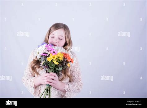 Smiling Twelve Year Old Girl With Long Dirty Blonde Hair Holding And Smelling Colorful Bouquet