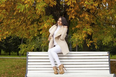 Beautiful Young Brunette Woman Sitting On A Bench In The Autumn Stock