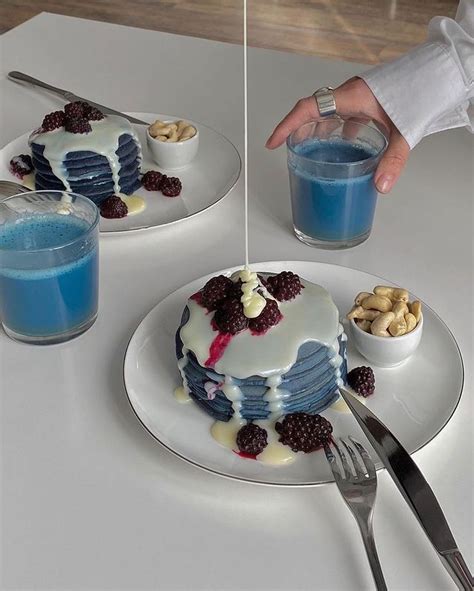 A Person Is Pouring Blue Liquid Onto A Cake On A Plate With Berries And